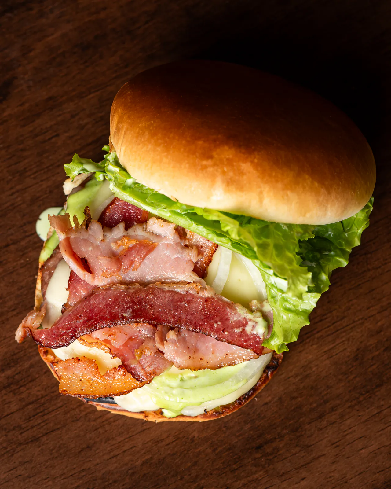 Pork Bacon Salada visto de cima, deitado sobre a mesa de madeira, com as camadas de bacon e alface à mostra.