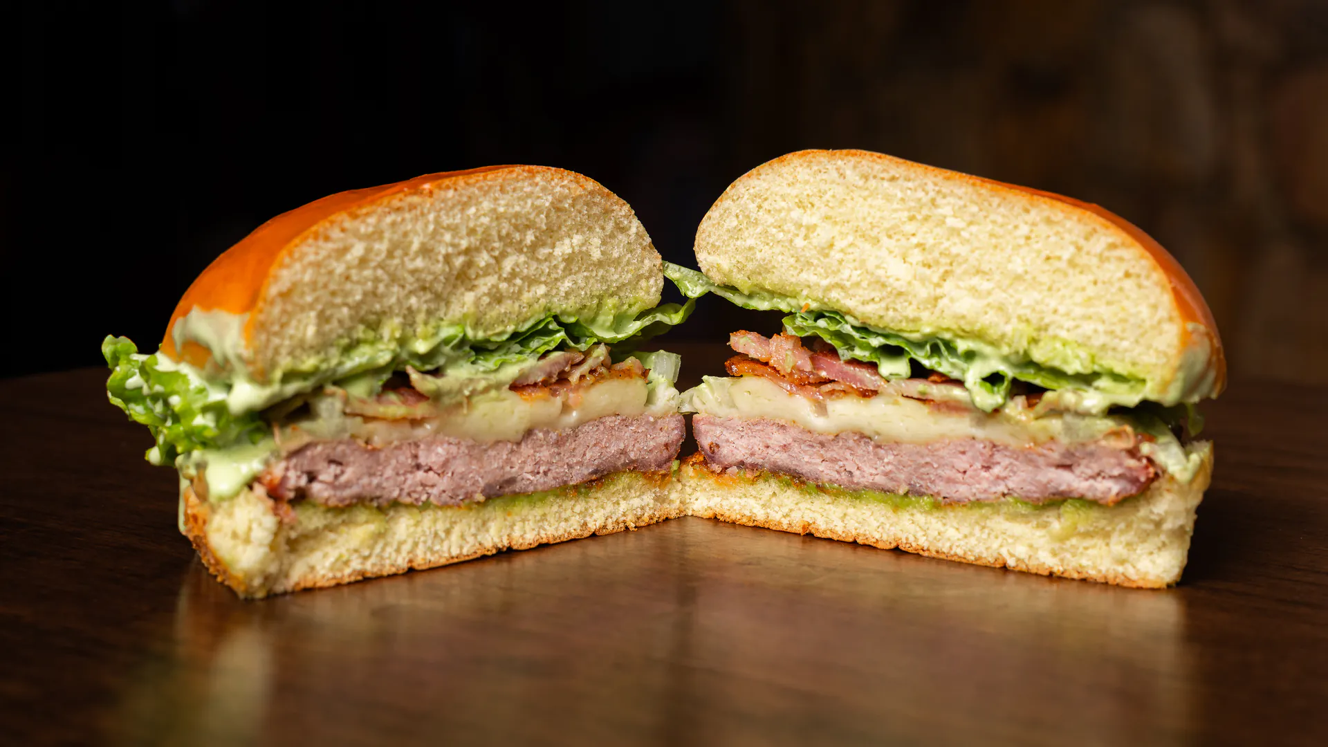 Pork Bacon Salada cortado ao meio: carne de pernil suíno rosada, queijo, bacon e alface entre o pão selado.